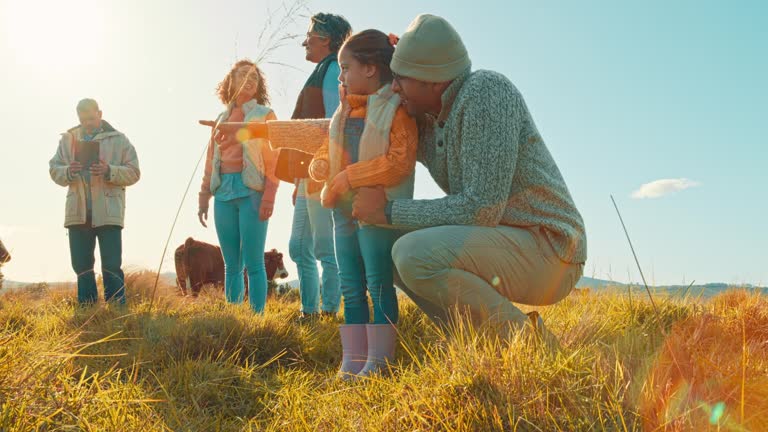 Nature, cattle and family on a farm bonding with a herd for livestock business in a field together. Happy, love and girl child standing with grandparents and parents by group of cows in countryside.