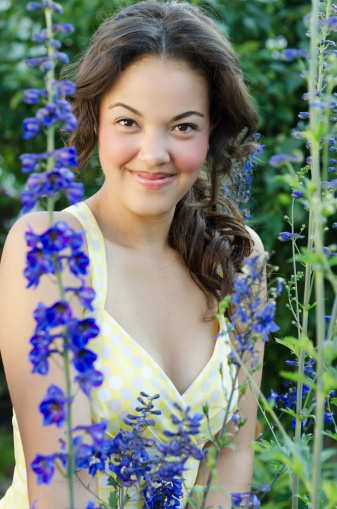 Vertical outdoor garden shot of smiling young woman among tall blue flowers.