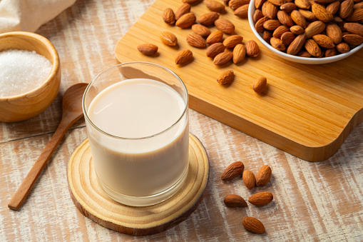 Almond milk in the glass with almond on wooden plate.