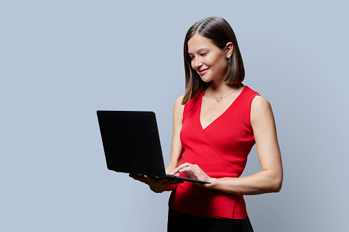 Smiling young business woman with laptop on grey studio background. Successful confident caucasian female looking at computer screen. Business, work, job, study, education, e-learning, technology