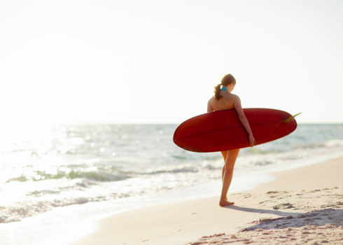 A young teenage girl carrying a surfboard walking on the beach.