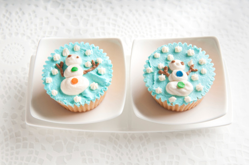 Close up of two cupcakes decorated with icing of a snowman surrounded by snowflakes.