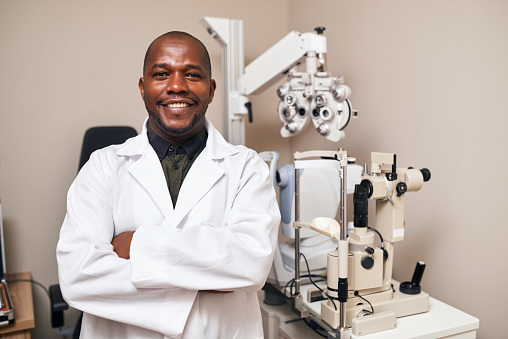 Happy, crossed arms and portrait of man optometrist in an optical clinic, store or shop for vision. Optometry, smile and African male optician with confidence and positive attitude for an appointment