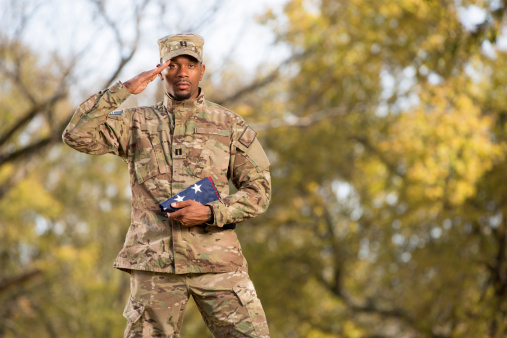 Kneeling Soldier Holding an American Flag Saluting. This stock image has a horizontal composition.