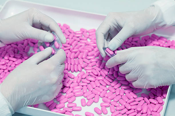 Two people sorting pink pills in a white tray stock photo