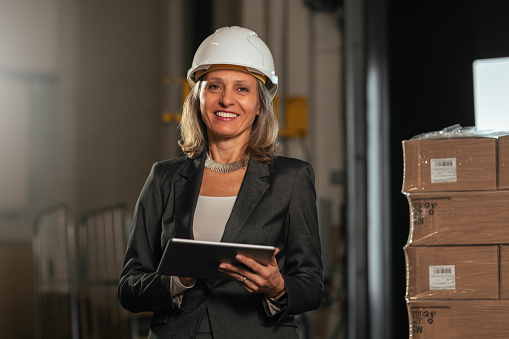 A businesswoman with a protective helmet using a digital tablet in a warehouse.