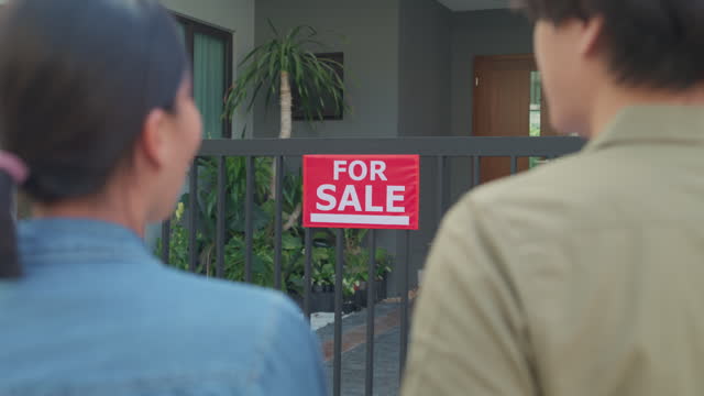Closeup of young Asian woman real estate broker showing house to client buyers outside at home. Buying a new house.