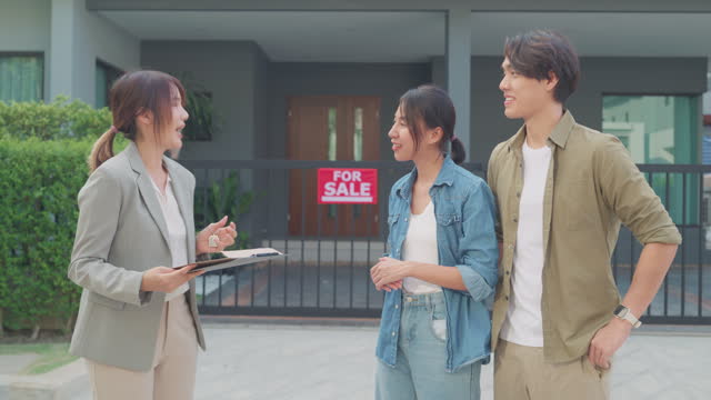 Young Asian woman real estate broker showing house to client buyers outside at home. Buying a new house.