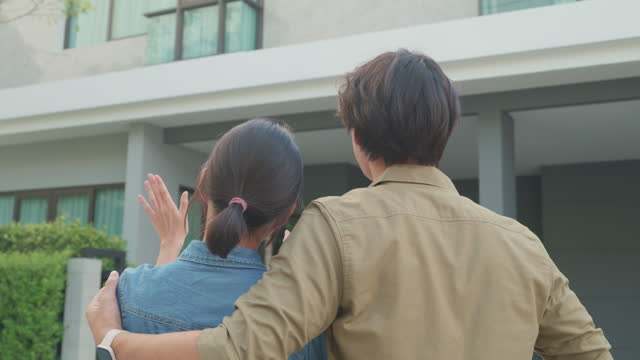 Closeup of young Asian couple standing and hugging together looking happy in front of their new house. Buying a new house.