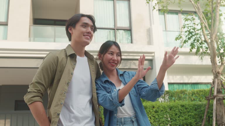 Young Asian couple standing and hugging together looking happy in front of their new house. Buying a new house.