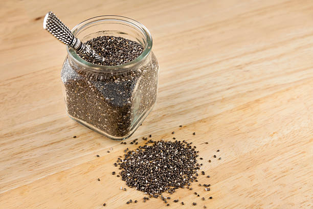 Chia Seeds in a jar Small jar of chia seeds with pile of seeds on a wood tabletop surface. Chia Seeds 1 Tbsp stock pictures, royalty-free photos & images