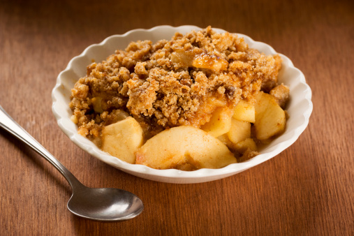 A bowl of freshly baked Apple Crisp (Apple Crumble) and a spoon. This dessert has a crumbly brown sugar topping over baked cinnamon apples. The apple crisp is in a small white bowl.