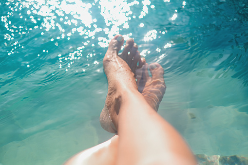 Close-up POV shot of unrecognizable woman legs crossed at ankle inside a swimming pool