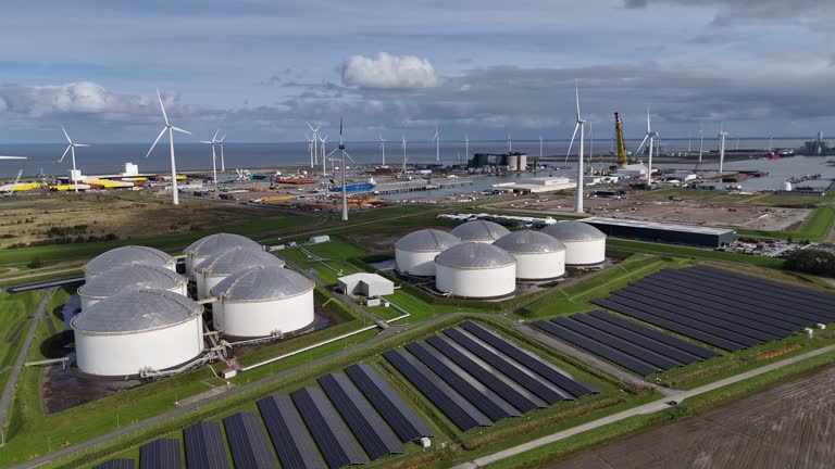 Solar panel park with windmills and fuel silos and harbor in background, Aerial