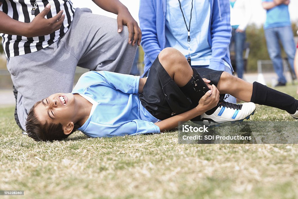 Giovane ragazzo tenendo una lesione alla caviglia durante la partita di calcio - Foto stock royalty-free di Lesionato