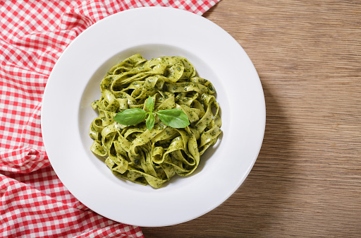 plate of pasta with pesto sauce on wooden background, top view