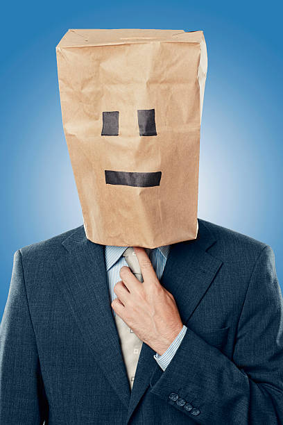 Anonymous businessman in suit with paper bag over his head Man wearing a suit and tie has his head covered by a brown paper bag. The bag has drawings of eyes and mouth. He looks very anonymous and is adjusting his necktie. anonymous businessman with paper bag on his head stock pictures, royalty-free photos & images