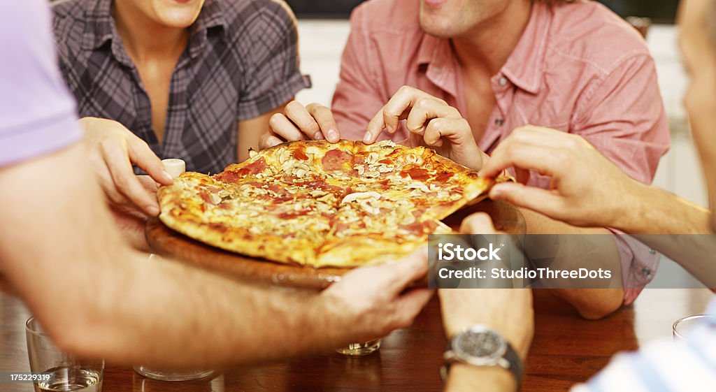 Gruppo di amici che condividono una pizza - Foto stock royalty-free di Abbigliamento casual