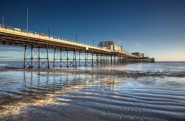 Worthing Pier reflected in wet sand at low tide, illuminated by late afternoon sunshine.