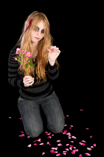 Vertical studio shot on black of blonde teen surrounded by fallen rose petals.