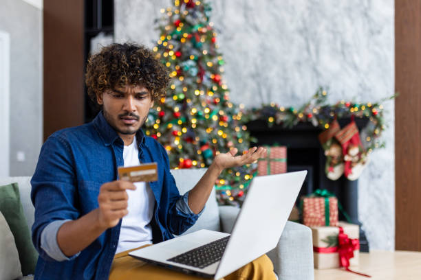 Upset cheated man lost money, refused to buy gift in online store, hispanic man using laptop and bank credit card for Christmas, upset and desperate, can't make money transfer. el hombre engañado molesto perdió dinero, se negó a comprar un regalo en la tienda en línea, el hombre hispano usa una computadora portátil y una tarjeta de crédito bancaria para navidad, molesto y desesperado, no puede hacer una transferencia de din