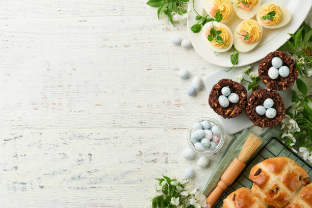 istock Easter brunch or breakfast. Easter chocolate nest cake with chocolate candy eggs, traditional hot cross buns and deviled eggs with bouquets of blooming apple trees. Spring Easter holiday food concept. 1752307699