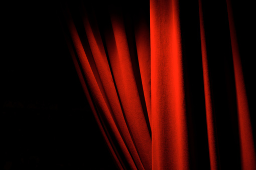 Theatrical red velvet curtains with dramatic lighting open to black copy space