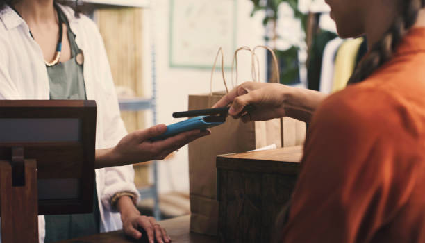 caixa, cliente e telefone com pdv na máquina, fintech ou pagamento digital em loja ou varejo de pequenas empresas. vendedores de pessoas, mãos e roupas, ponto de venda no aplicativo móvel, torneira e saco de compras - clothing store sales clerk usa clothing - fotografias e filmes do acervo