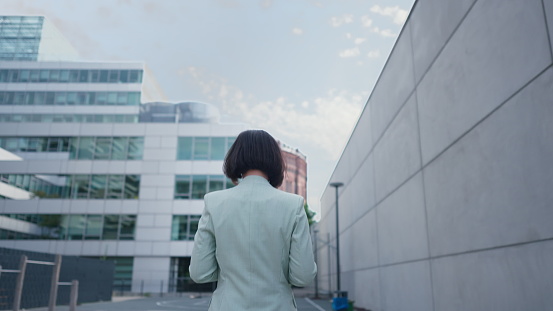 Back view of the business woman walking to the work after break. Modern building, financial center, cityscape. Successful female businessperson concept
