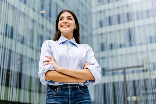 Confidence portrait of young businesswoman standing over office building. Leadership, vision and empowerment concept.