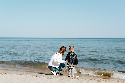 Mom and daughter together at sea. A young mother with a child on the shore on a sunny day, view from the back.