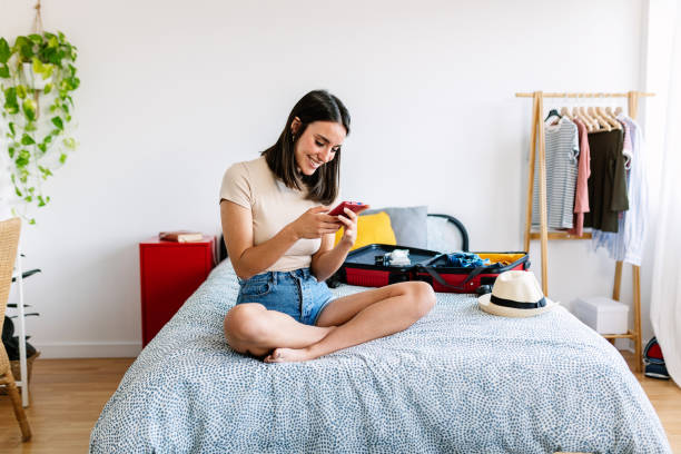 istock Young pretty woman using smartphone while preparing travel suitcase 1752336434