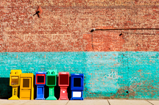 Various newspaper racks agains brick wall