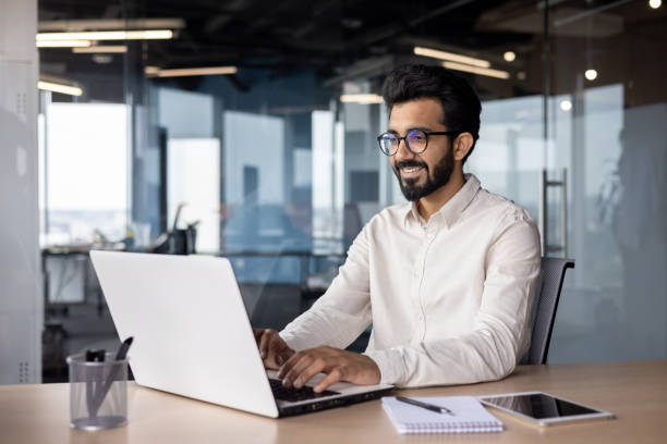 istock A young smiling Indian man is working in the office on a laptop, texting, chatting 1752338523