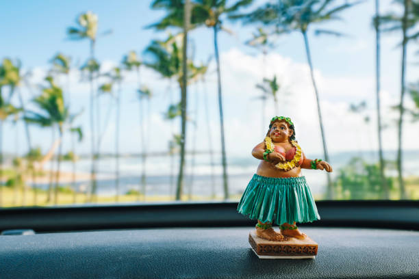 Hawaiian Hula dancer doll sitting on car dashboard with beach and palm trees in background