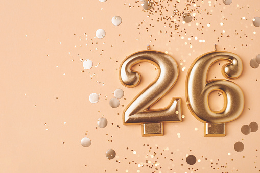 26 years celebration. Greeting banner. Gold candles in the form of number twenty six on peach background with confetti.