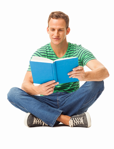 Full length of a young man in casual wear sitting cross-legged reading book on floor. Vertical shot. Isolated on white.