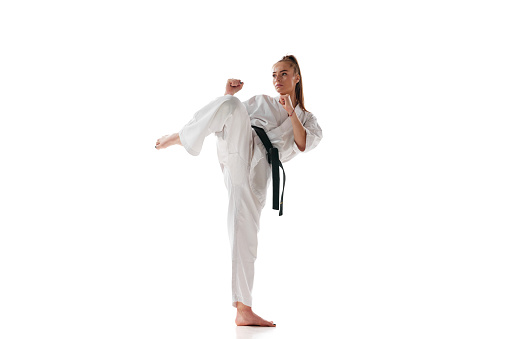 Rear view. Woman professional karate fighter in uniform performing kick in action isolated over white background. Concept of sport, recreation, art, hobby, culture. Copy space for ad, text.