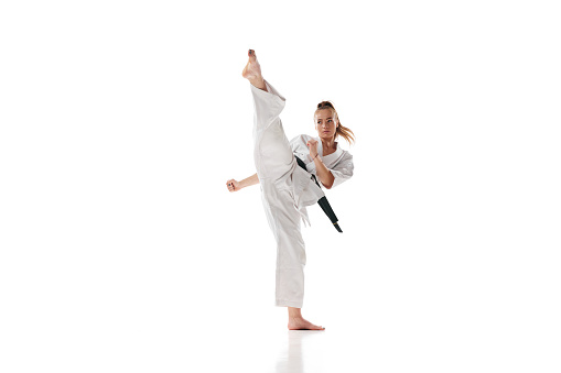 Woman in white sport karate uniform with black belt training in action against white studio background. Concept of professional sport, recreation, art, hobby, culture. Copy space for ad.