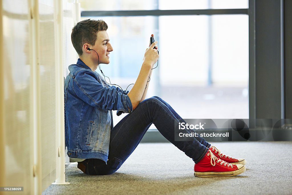 Cool teenager listening to music whilst texting on mobile Cool teenager sitting on floor listening to music from phone whilst texting on mobile 20-29 Years Stock Photo