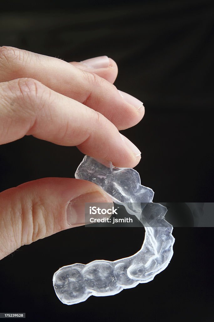 Dispositivos de Dental, en los dedos sobre fondo oscuro - Foto de stock de Ortodoncia invisible libre de derechos