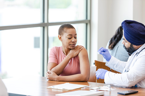 A young woman watches as a doctor prepares to give her a COVID-19 booster dose.