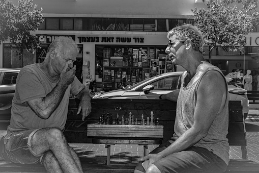 Tel Aviv, Israel – August 04, 2023: The two adult male friends enjoying a conversation in front of a shop.