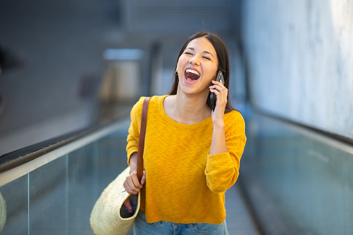 Portrait laughing young woman standing on escalator with cellphone
