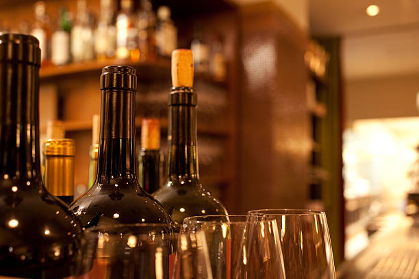 Wine bar with bottles and crystal glasses "Red wine bottles and crystal glasses on a bar counter, with blurred background and copy space, warm atmosphere." wine bar counter stock pictures, royalty-free photos & images