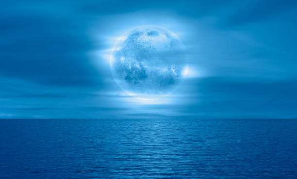 istock Night sky with blue moon in the clouds over the calm blue sea 