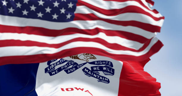 Close-up of Iowa state flag waving in the wind with the US flag on a clear day Close-up of Iowa state flag waving in the wind with the American national flag on a clear day. 3d illustration render. Rippled fabric. Selective focus iowa flag stock pictures, royalty-free photos & images