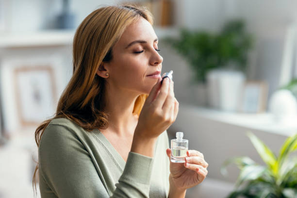 hermosa mujer chica sosteniendo una botella de aceite esencial mientras la prueba sentada en un sofá en casa. - aromaterapia fotografías e imágenes de stock