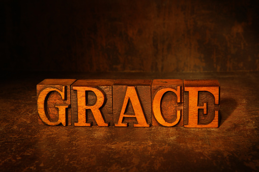 Grace spelled out in vintage wooden letterpress letters on a grunge background, lit with tungsten lighting.