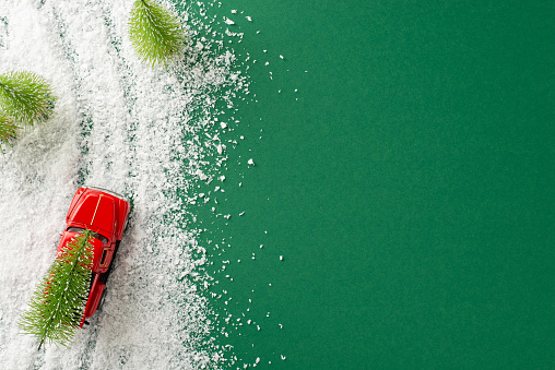Embrace New Year's magic. Top view photo of a little car transporting a Christmas tree through a snowy landscape on a green background, providing room for your holiday wishes or promotions
